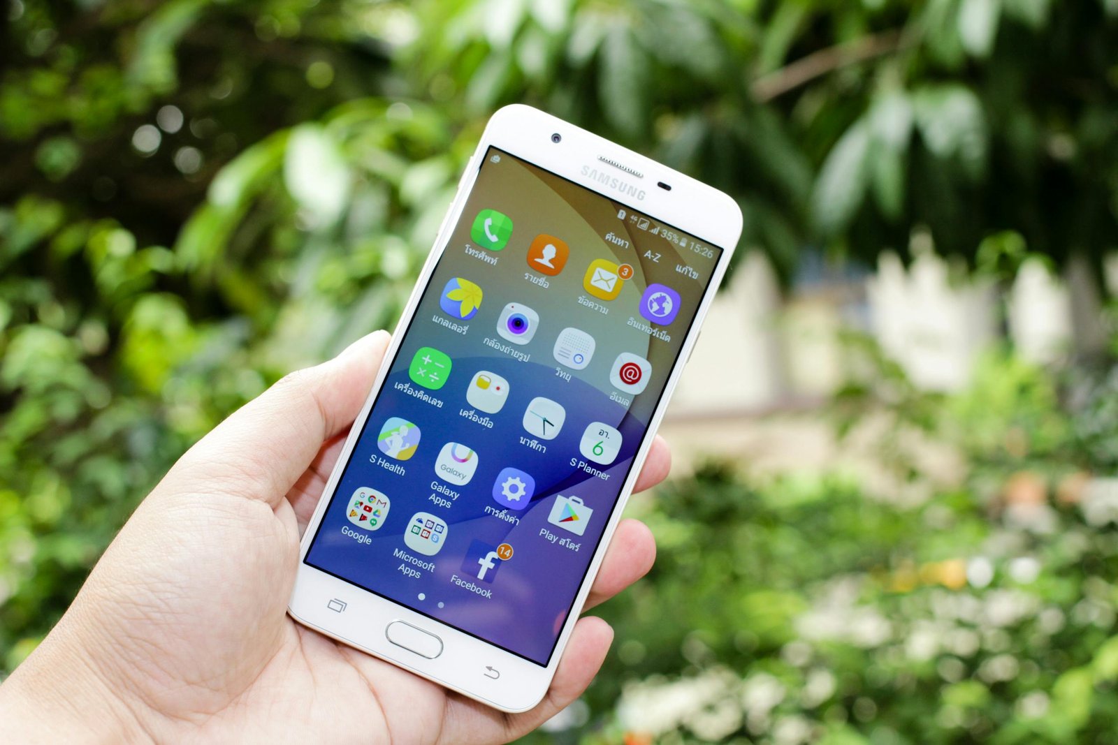close up of a hand holding a smartphone displaying various app icons against a blurred outdoor backg